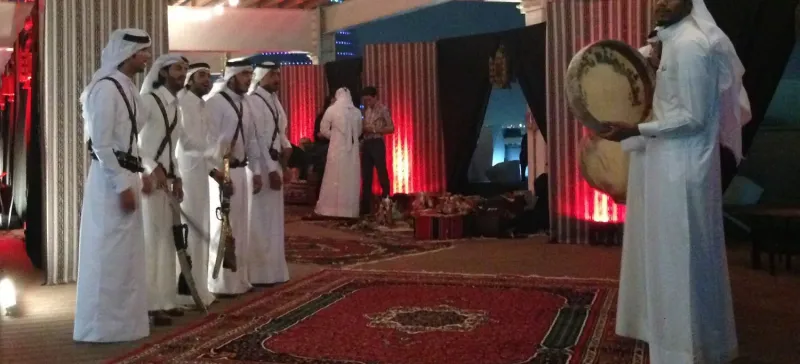 Men in traditional dress performing a heritage dance in a red-lit tent