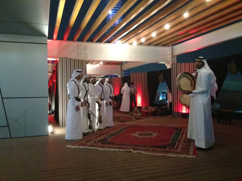 Men in white thobes performing with drums on a carpeted heritage stage