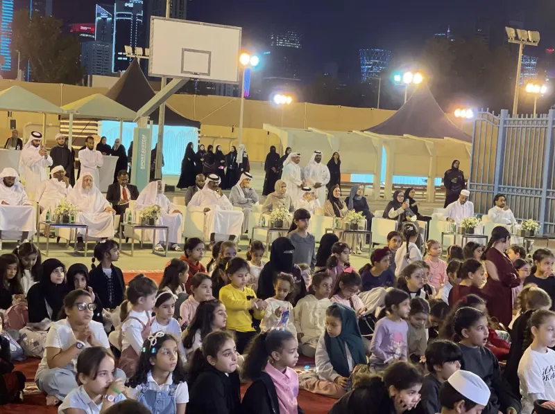 Children and families seated on grass at an evening outdoor event