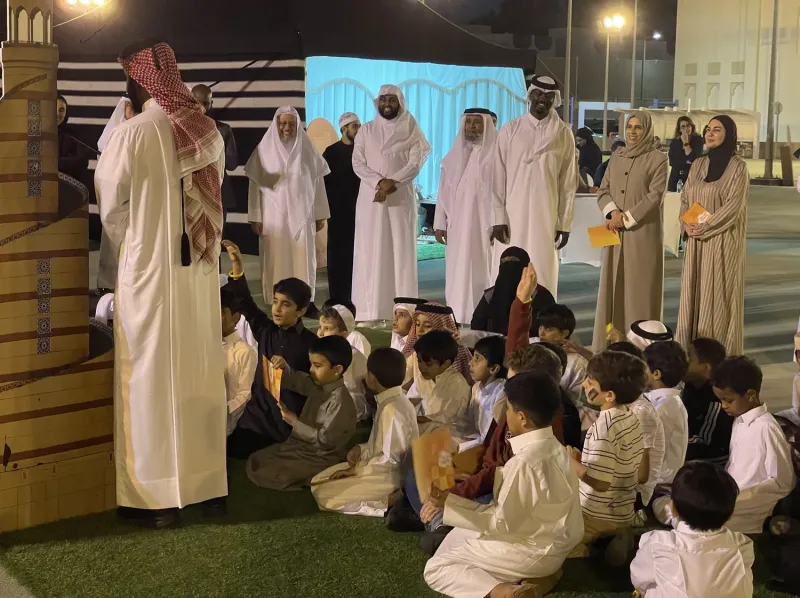 Speaker addressing seated children and guests at an outdoor evening gathering