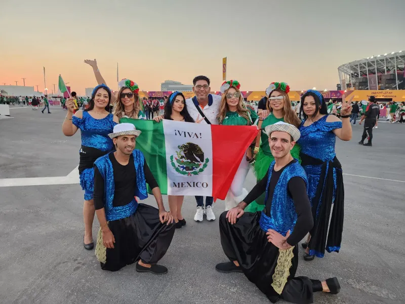 Performers in blue costumes posing with flag-waving fans at a World Cup fan zone