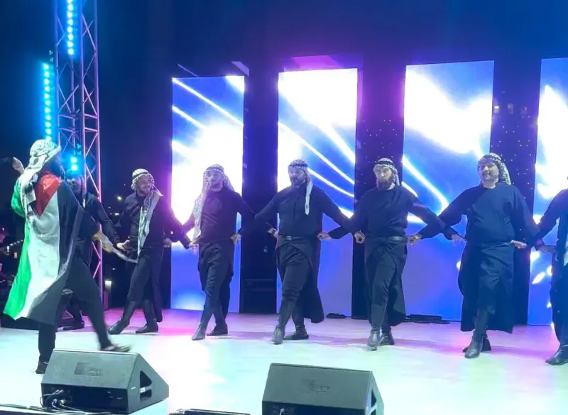 Male folk dance troupe performing on a lit stage with LED screens