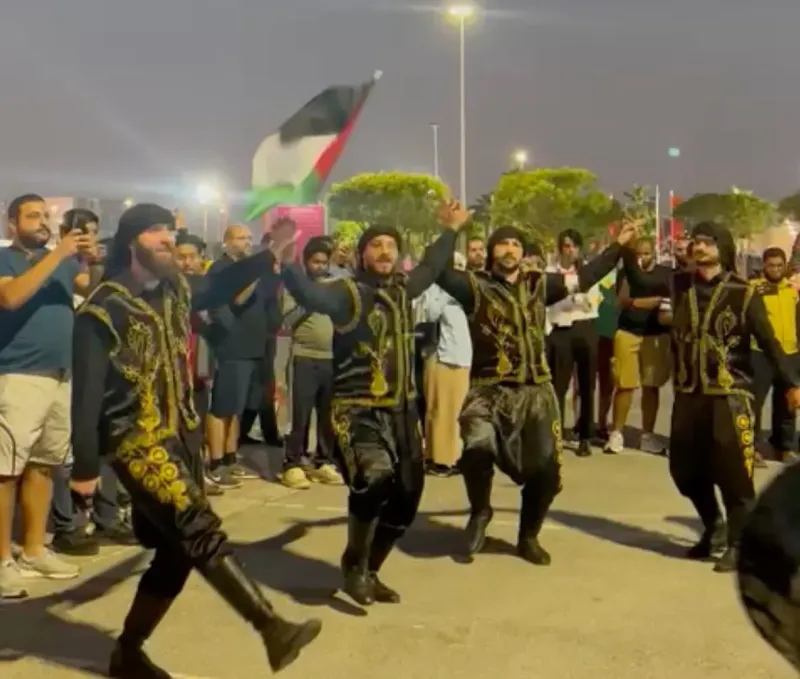Performers in gold-embroidered costumes dancing among cheering fans at the fan zone
