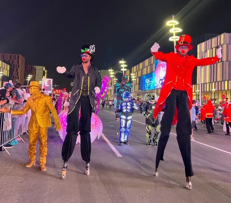Stilt walkers in gold and red costumes performing before crowds at night