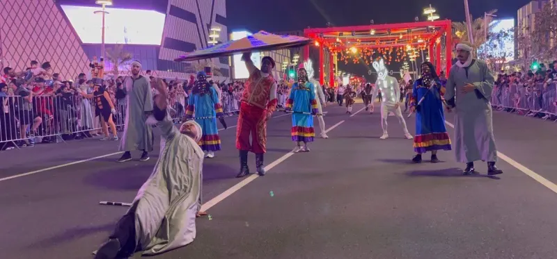 Parade of stilt walkers and performers along a barricaded street at night