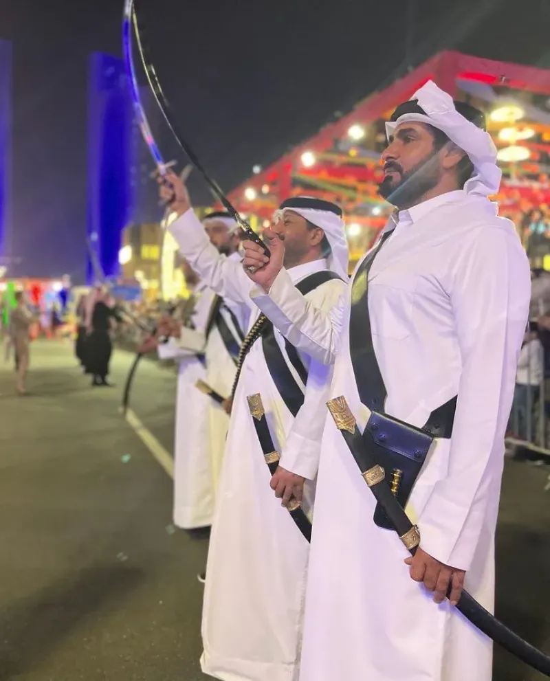 Men in traditional white thobes performing a sword dance on a closed street at night