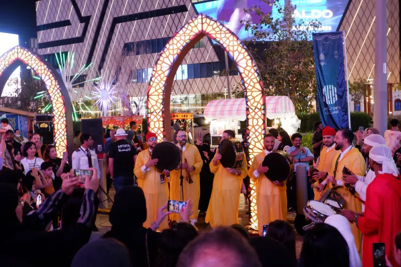 Folk drummers in yellow costumes performing beneath illuminated Ramadan arches