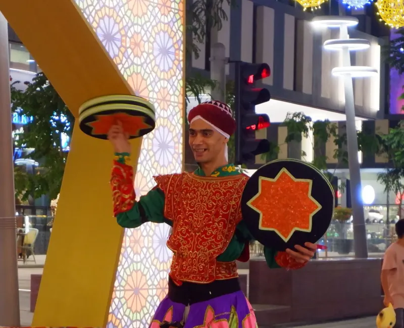 Performer in embroidered costume balancing decorative trays beside patterned arch lights