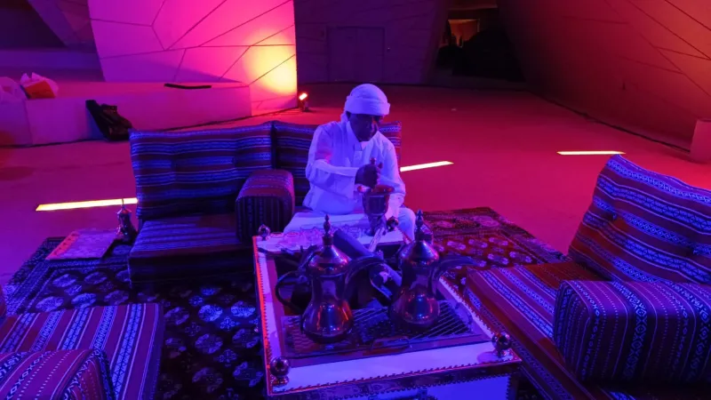 Performer seated on majlis cushions under magenta and blue stage lighting