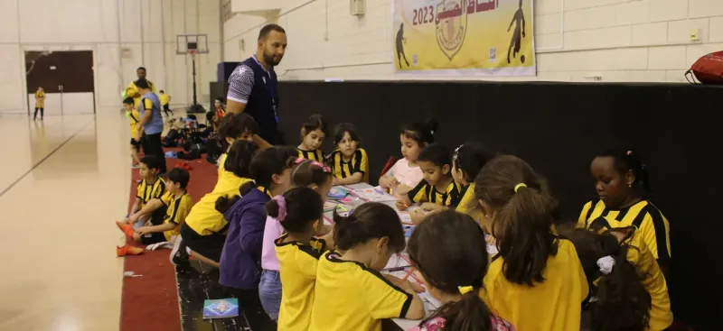Children in yellow camp shirts working at long activity tables in a sports hall