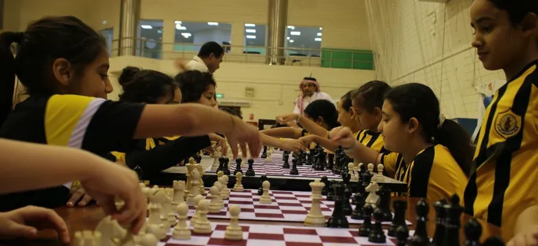 Children in camp uniforms playing chess side by side at long tables