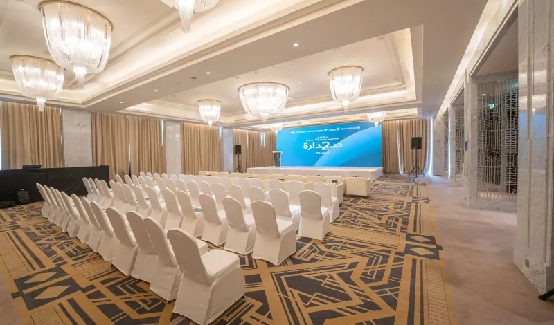 Hotel ballroom with rows of white chairs facing a branded stage