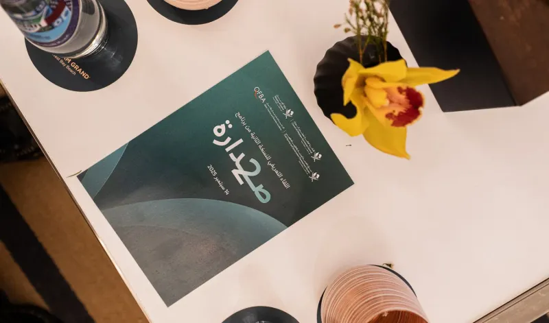 Printed Sadara 2 programme booklet beside a flower on a table