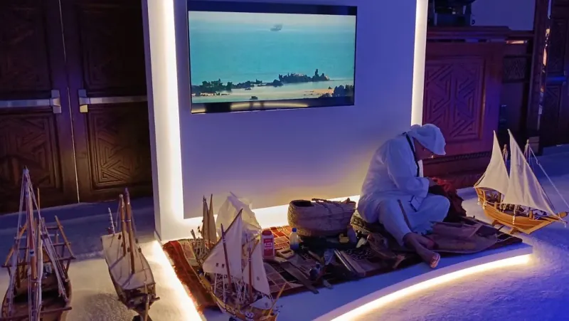 Cultural display of traditional dhow models and a craftsman in an illuminated booth