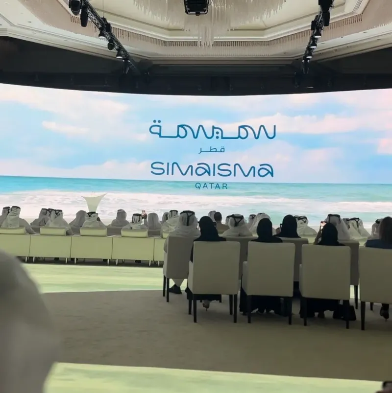 Audience seated before a wide LED screen showing the Simaisma project logo