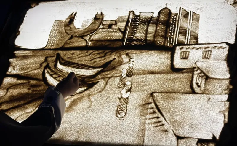 Sand art scene of traditional boats and waterfront buildings on a light table