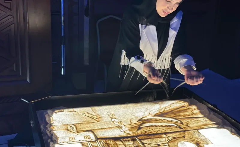 Sand artist drawing a landscape on a lit sand table at a launch event