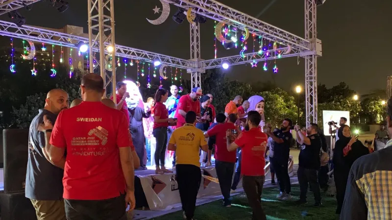 Staff in red shirts and families on a festival stage under crescent lights