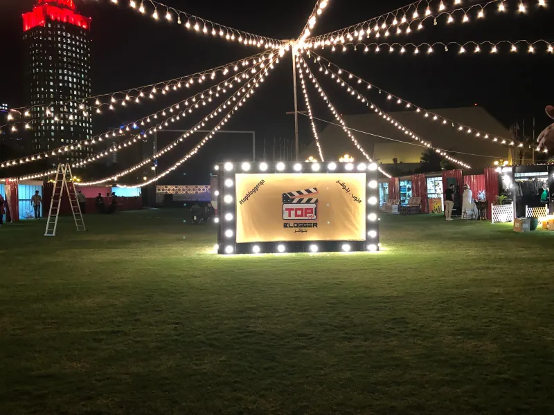 Illuminated Top Blogger clapperboard sign on a lawn under festival string lights