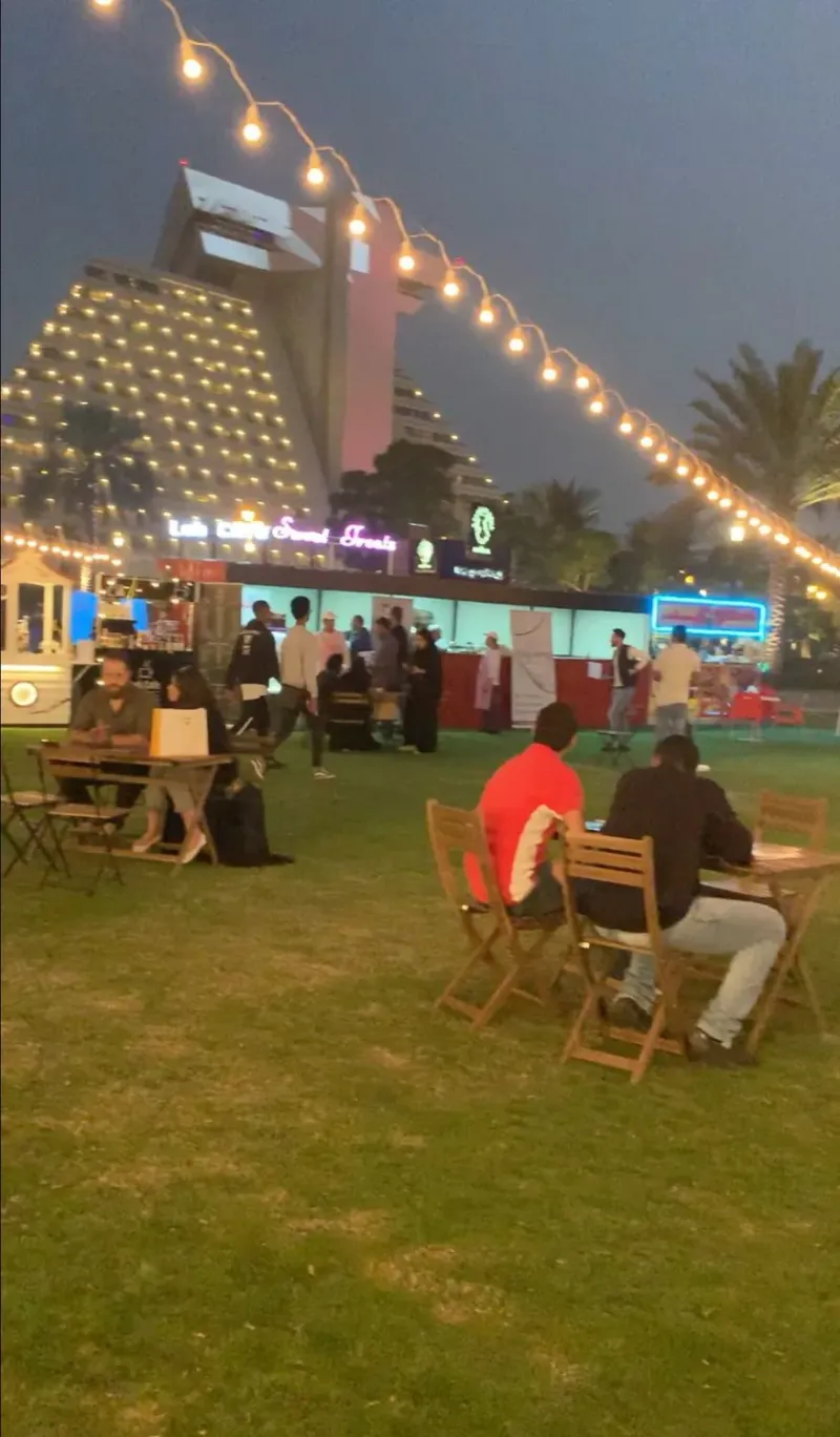 Outdoor lawn seating area at dusk with string lights and a hotel tower behind