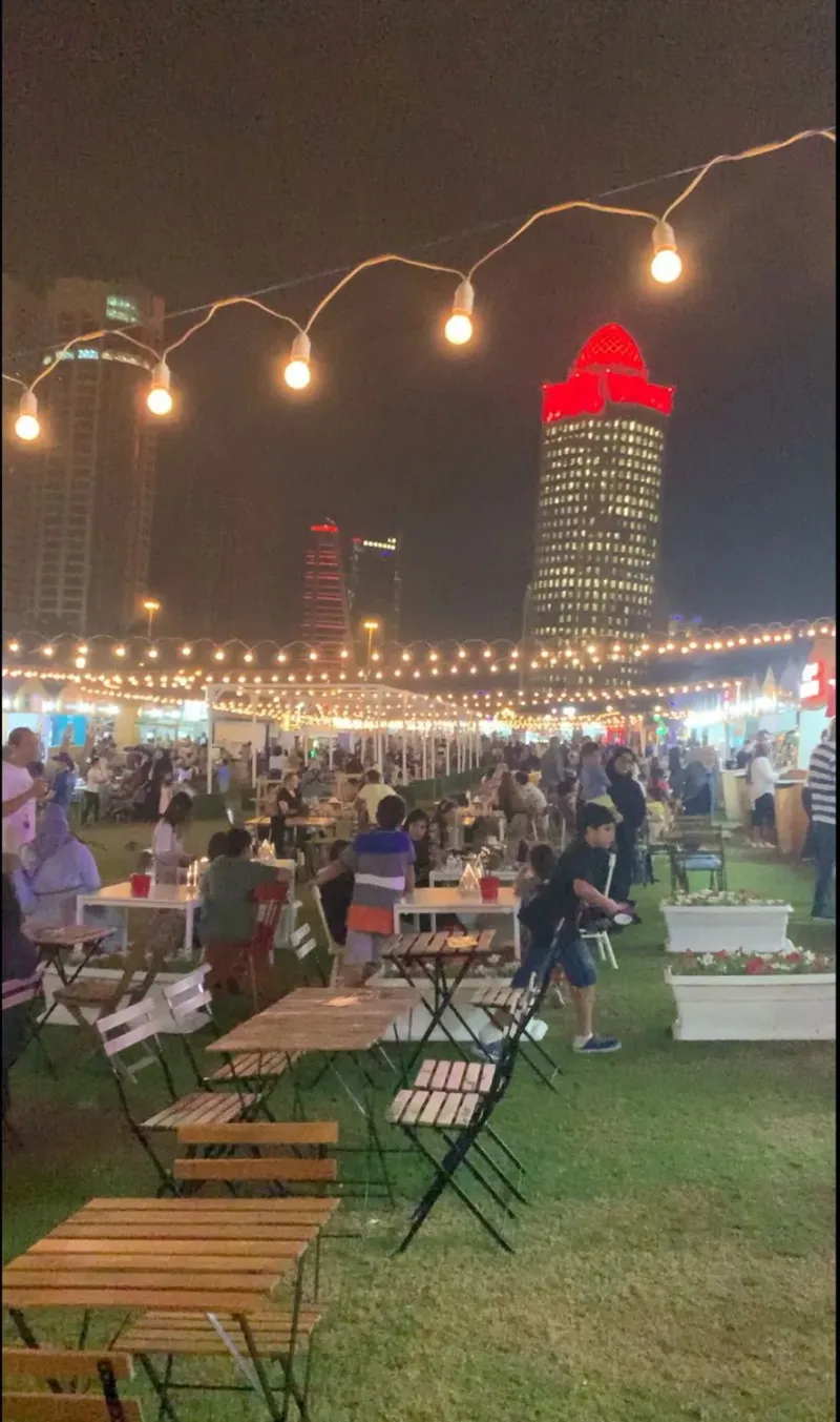 Outdoor seating area under string lights at a festival with city lights beyond
