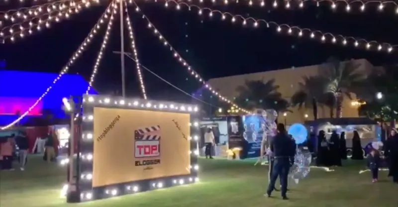 Festival lawn lit by string lights with clapperboard sign and visitors at night